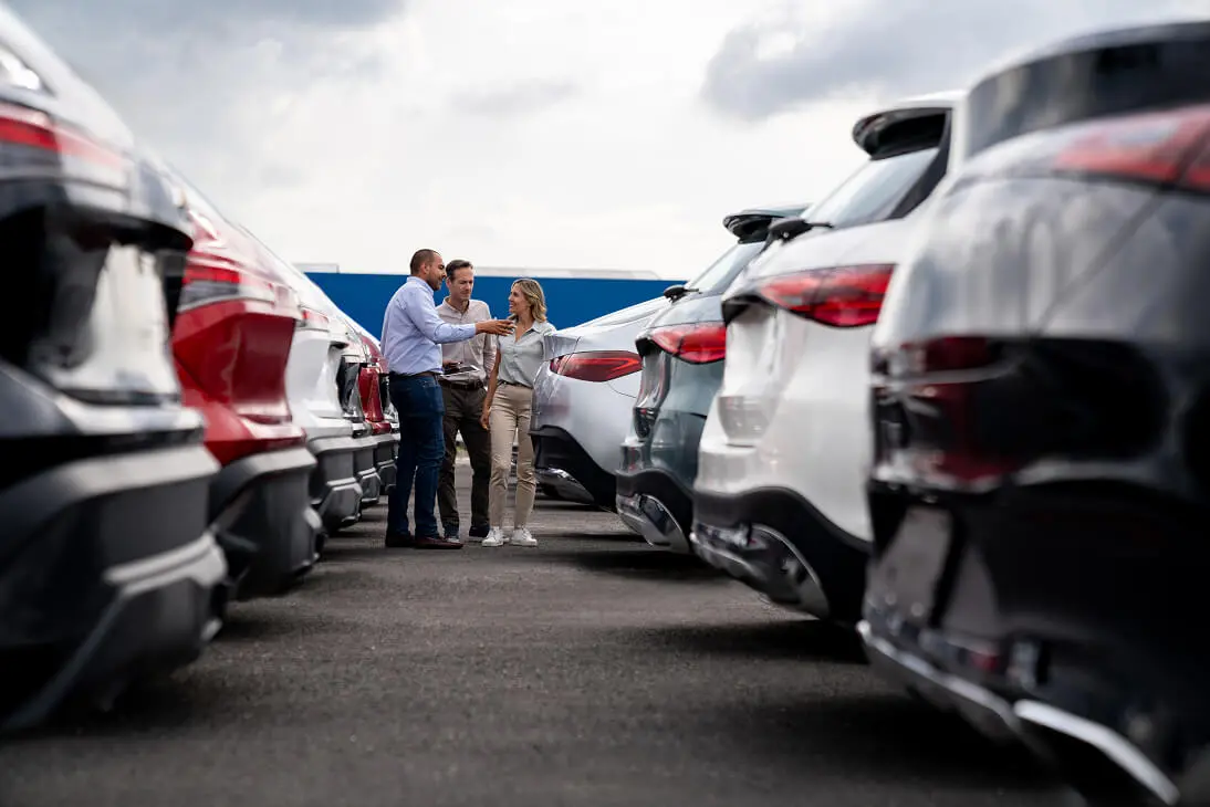 Car dealership lot with people discussing vehicles.